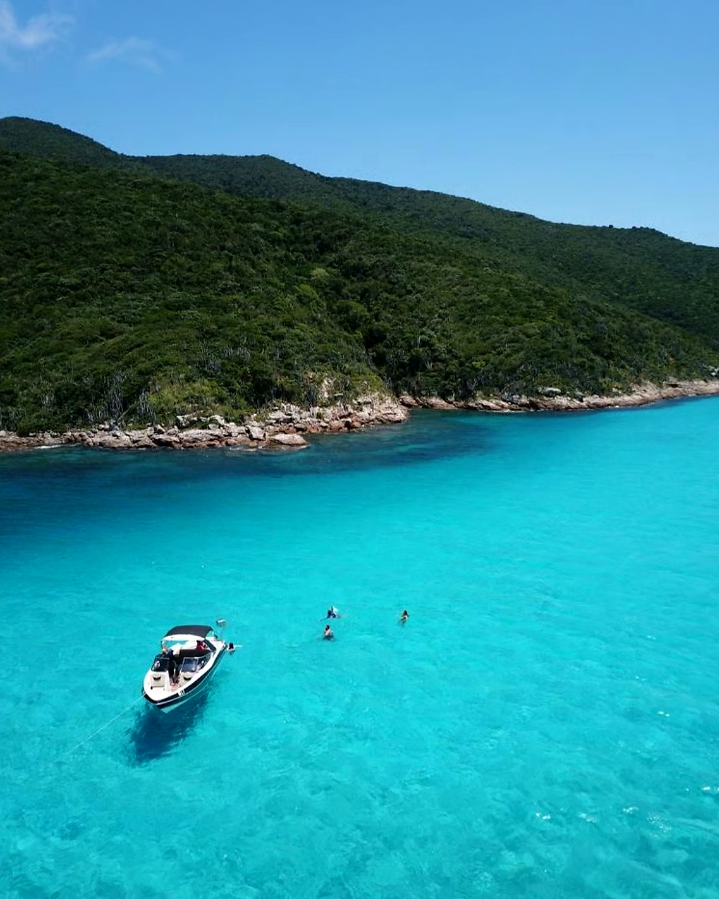 Embarcação ancorada em água verde-cristalina junto a uma ilha de mata atlântica